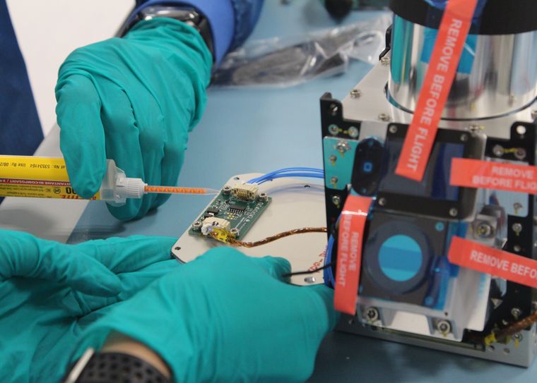 Gloved hands applying adhesive to a circuit board next to a flight module
