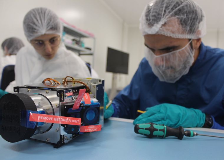 Two engineers in clean-room gear working on a flight module